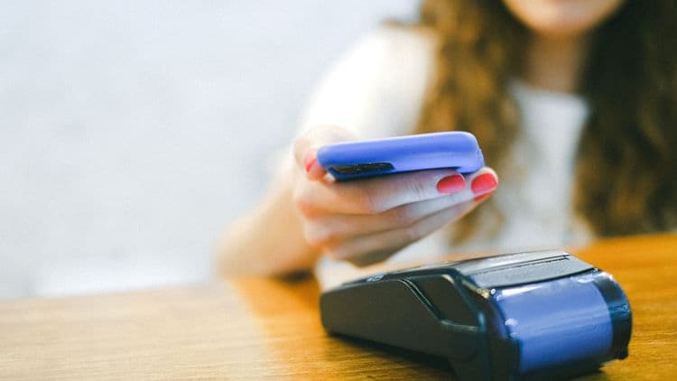 Eine Person hält ein Smartphone über ein Kartenterminal an einer Kasse.