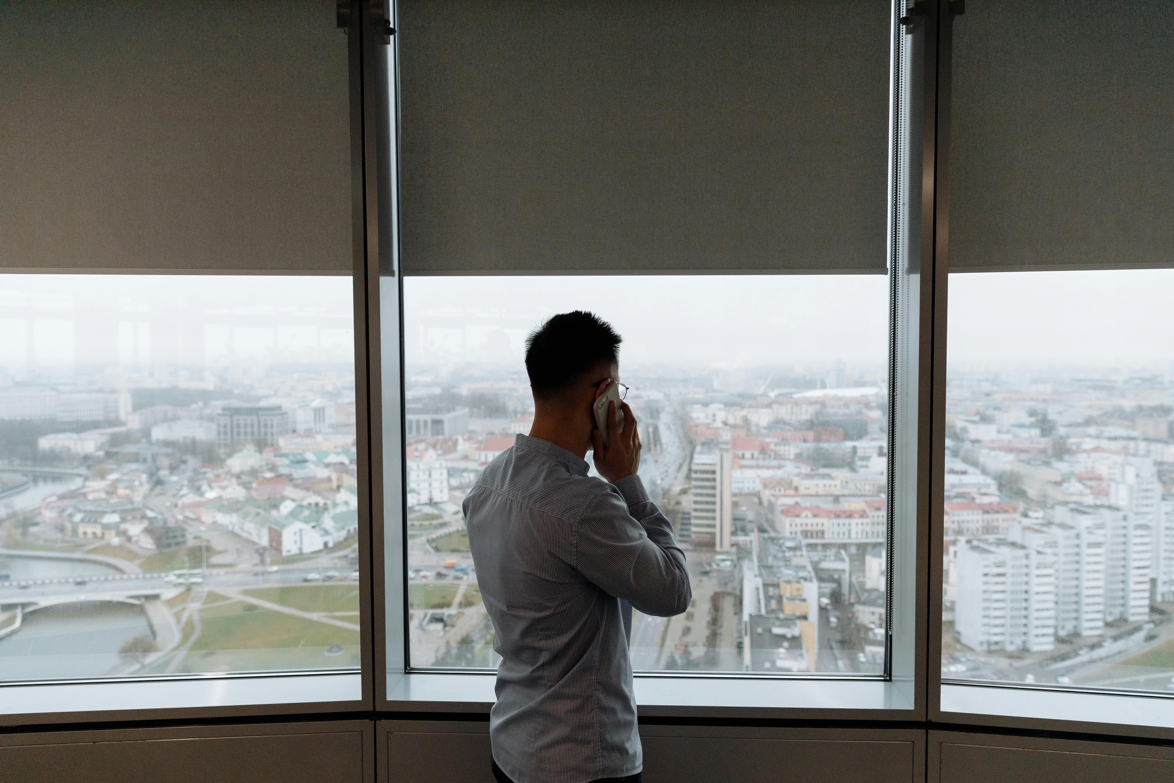 Ein Mann telefoniert vor einer großen Fensterfront mit Blick über eine Stadt.